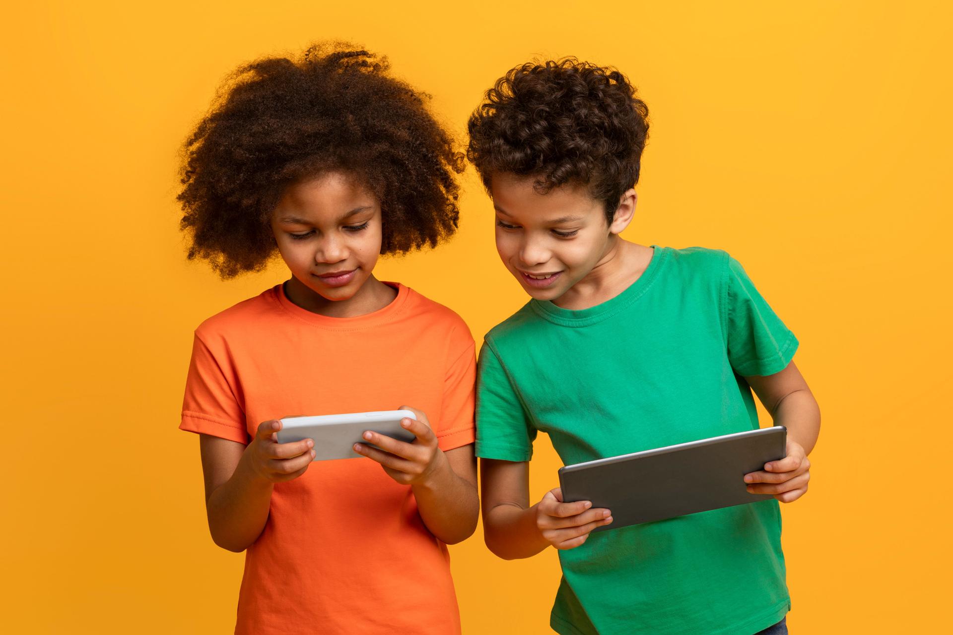 Two Children Using a Tablet Computer on a Yellow Background
